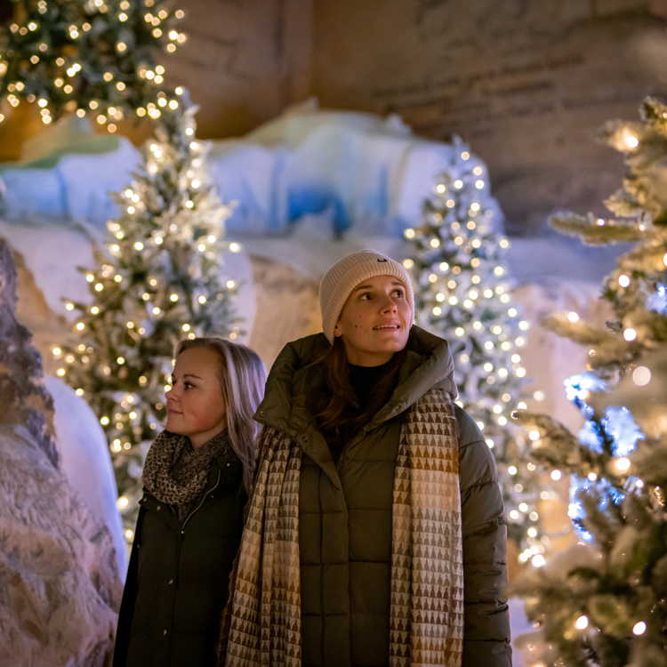 2 vrouwen kijken om zich heen in een winters versierde kerstgrot