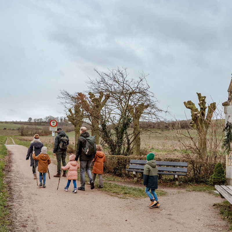 Volwassenen en kinderen lopen weg van kapelletje in Zuid-Limburgs landschap