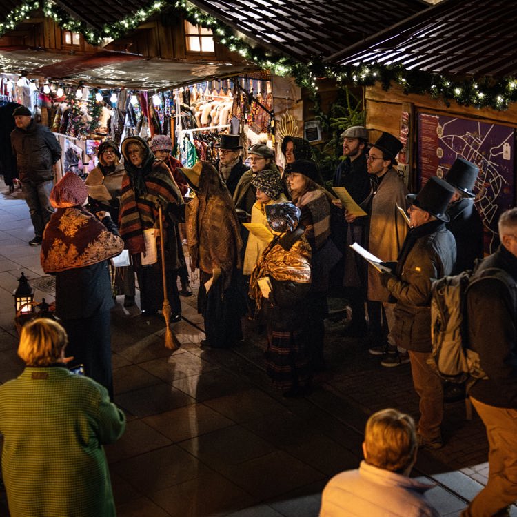 Een koor in Dickens kostuums zingt te midden van kerstkraampjes in de avond